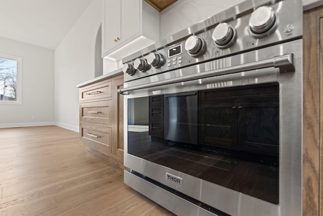 kitchen featuring white cabinets, wall oven, light wood-type flooring, and vaulted ceiling