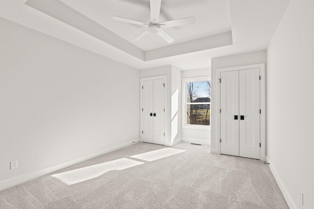 unfurnished bedroom with light colored carpet, a raised ceiling, and ceiling fan