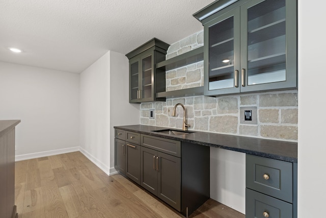 kitchen featuring backsplash, dark stone counters, sink, light hardwood / wood-style flooring, and a textured ceiling