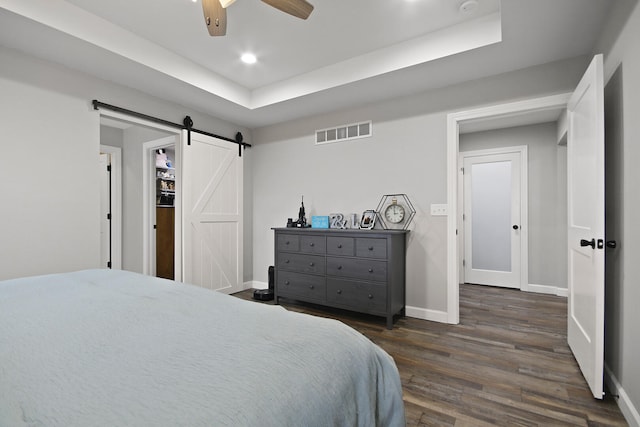 bedroom with ceiling fan, a barn door, a tray ceiling, and dark hardwood / wood-style flooring