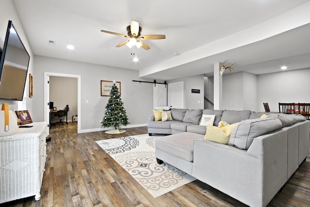 living room featuring dark hardwood / wood-style flooring, ceiling fan, and a barn door