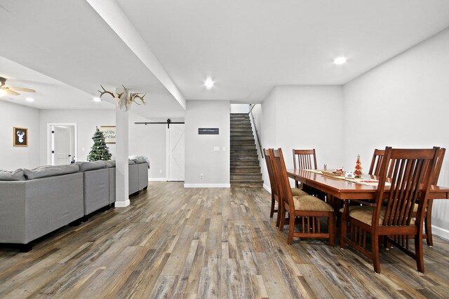 dining area with ceiling fan, a barn door, and dark wood-type flooring