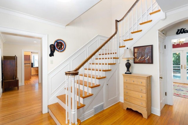 stairway with crown molding, french doors, and wood-type flooring