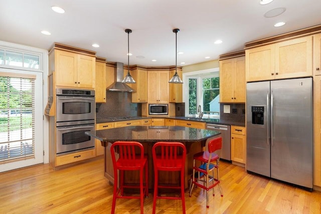 kitchen with decorative light fixtures, stainless steel appliances, a kitchen island, and wall chimney range hood