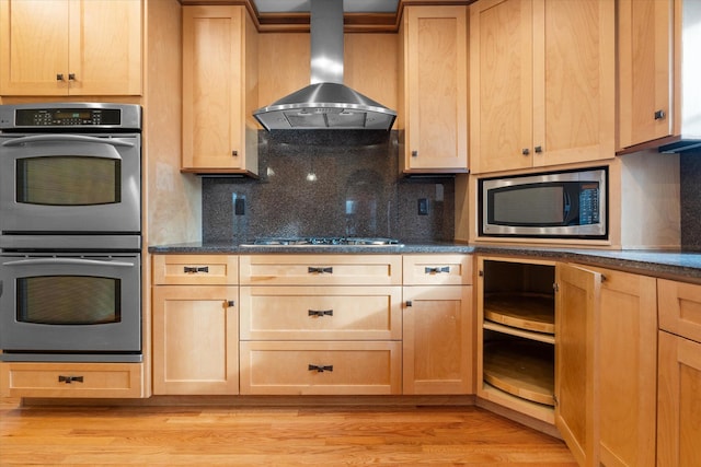 kitchen with decorative backsplash, appliances with stainless steel finishes, light hardwood / wood-style floors, and wall chimney range hood