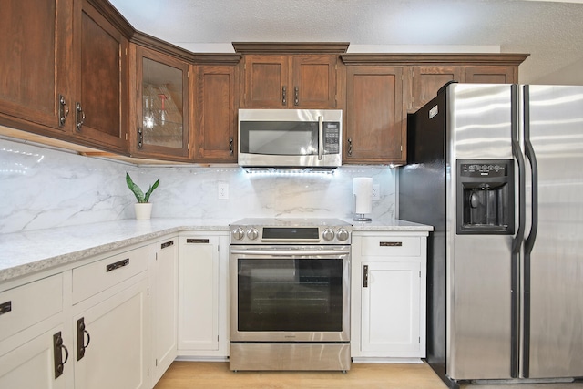 kitchen featuring backsplash, white cabinetry, light stone countertops, and appliances with stainless steel finishes