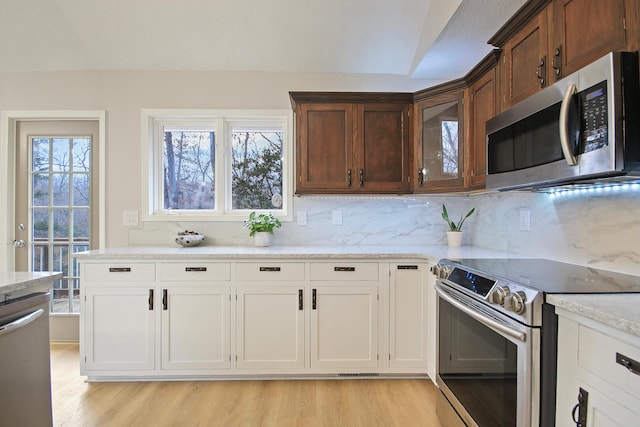 kitchen with light wood-type flooring, backsplash, stainless steel appliances, a healthy amount of sunlight, and white cabinetry