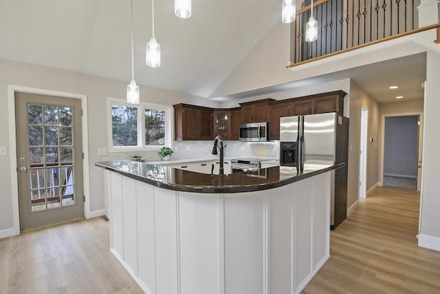 kitchen with appliances with stainless steel finishes, dark brown cabinets, a kitchen island with sink, high vaulted ceiling, and hanging light fixtures