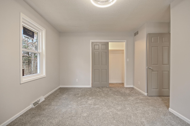 unfurnished bedroom featuring a walk in closet, a closet, light colored carpet, and a textured ceiling