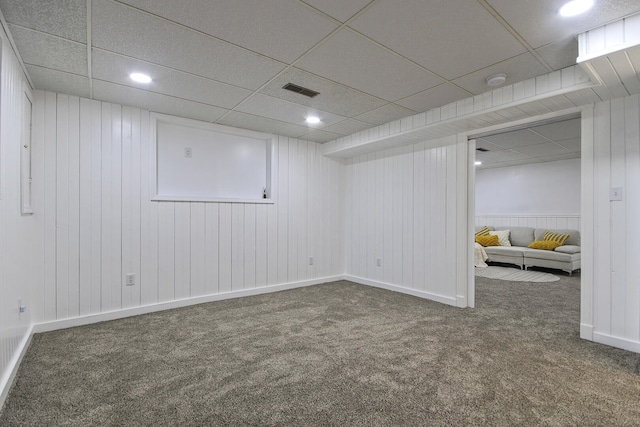 basement featuring wood walls, a drop ceiling, and dark carpet