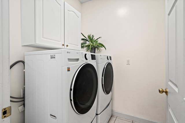 laundry room with cabinet space, light tile patterned floors, baseboards, and washing machine and clothes dryer