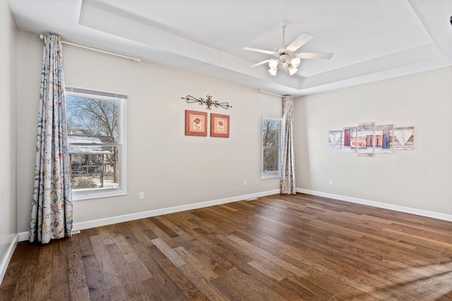 empty room featuring a tray ceiling, wood finished floors, a ceiling fan, and baseboards