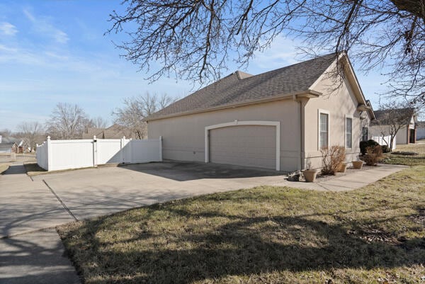 view of home's exterior with stucco siding, an attached garage, a gate, fence, and driveway