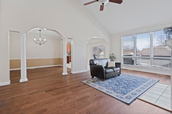 living area with decorative columns, arched walkways, wood finished floors, and ceiling fan with notable chandelier