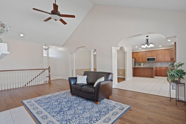 sitting room featuring arched walkways, recessed lighting, light wood-style flooring, an upstairs landing, and ceiling fan with notable chandelier