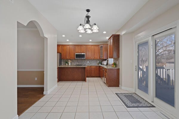 kitchen featuring light tile patterned floors, stainless steel microwave, backsplash, and glass insert cabinets