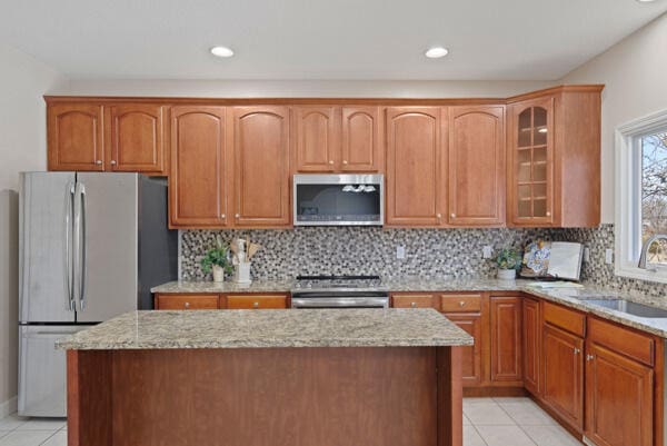 kitchen featuring light tile patterned floors, appliances with stainless steel finishes, light stone counters, a center island, and a sink