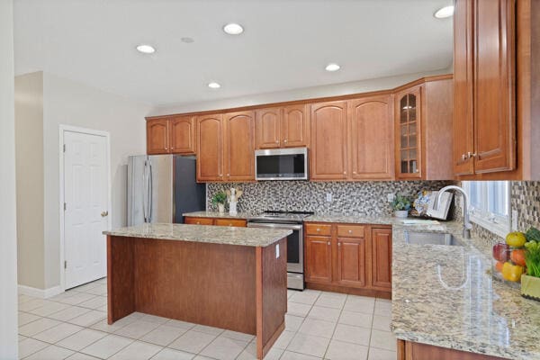 kitchen featuring light stone countertops, appliances with stainless steel finishes, backsplash, and a sink