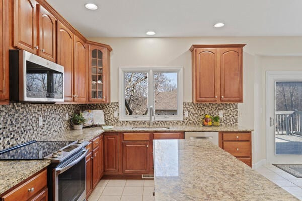 kitchen featuring a wealth of natural light, appliances with stainless steel finishes, light tile patterned flooring, a sink, and light stone countertops