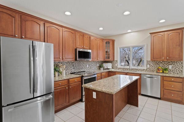 kitchen featuring light tile patterned floors, glass insert cabinets, appliances with stainless steel finishes, light stone counters, and a sink