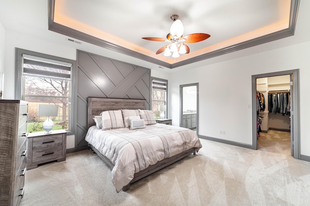 bedroom featuring light carpet, a raised ceiling, ceiling fan, a spacious closet, and a closet