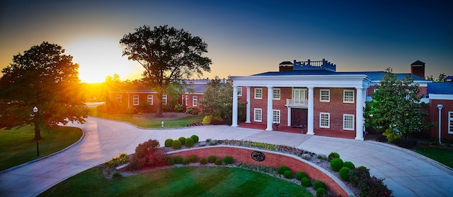 neoclassical home with a chimney, a front yard, concrete driveway, and a balcony