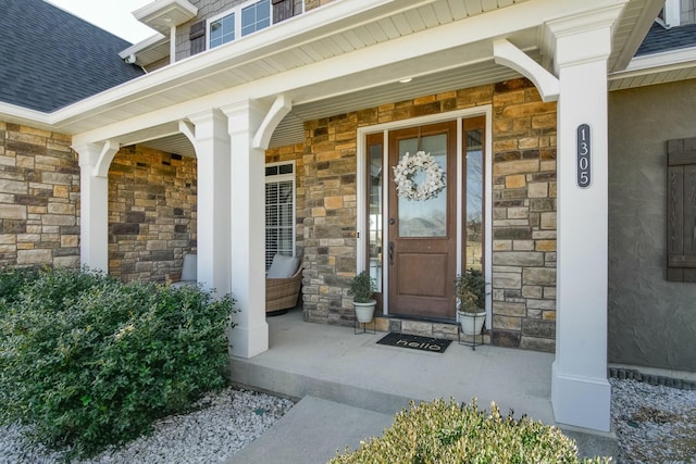 view of exterior entry with covered porch, stone siding, and roof with shingles