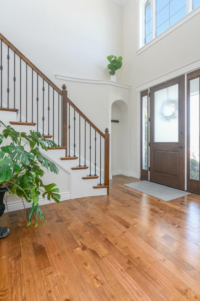 entryway with stairway, a high ceiling, arched walkways, and wood finished floors