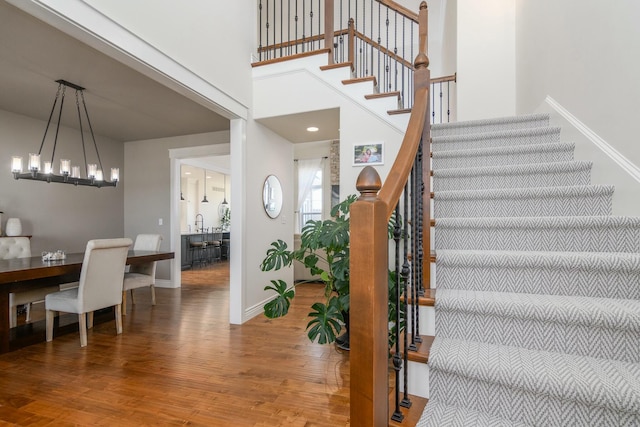 stairway featuring a towering ceiling, an inviting chandelier, baseboards, and wood finished floors