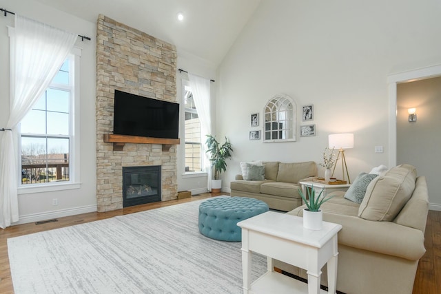 living room featuring high vaulted ceiling, a stone fireplace, wood finished floors, and baseboards