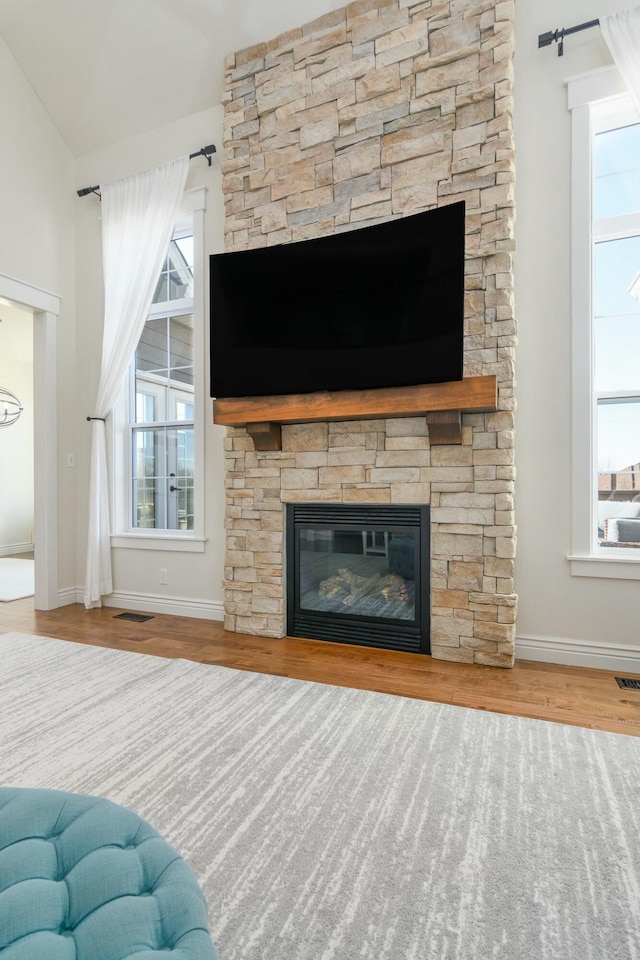 unfurnished living room with a stone fireplace, wood finished floors, visible vents, baseboards, and vaulted ceiling