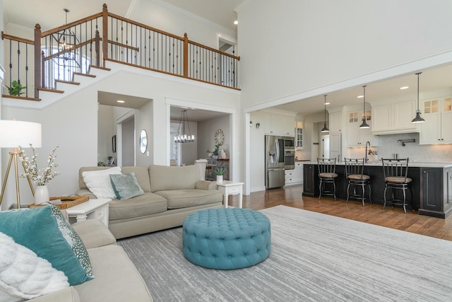 living room with a towering ceiling, ornamental molding, stairway, dark wood-style floors, and an inviting chandelier