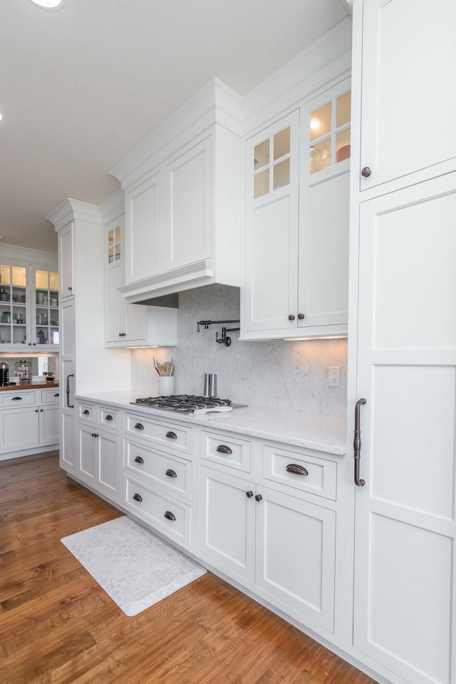 kitchen featuring stainless steel gas cooktop, light countertops, glass insert cabinets, white cabinetry, and light wood-type flooring