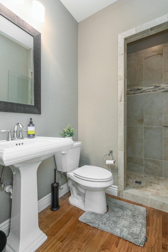 bathroom with baseboards, a tile shower, toilet, and wood finished floors