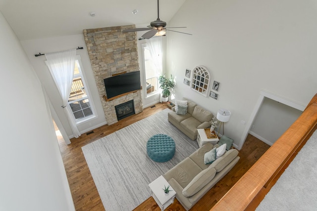 living room featuring high vaulted ceiling, a stone fireplace, wood finished floors, visible vents, and baseboards