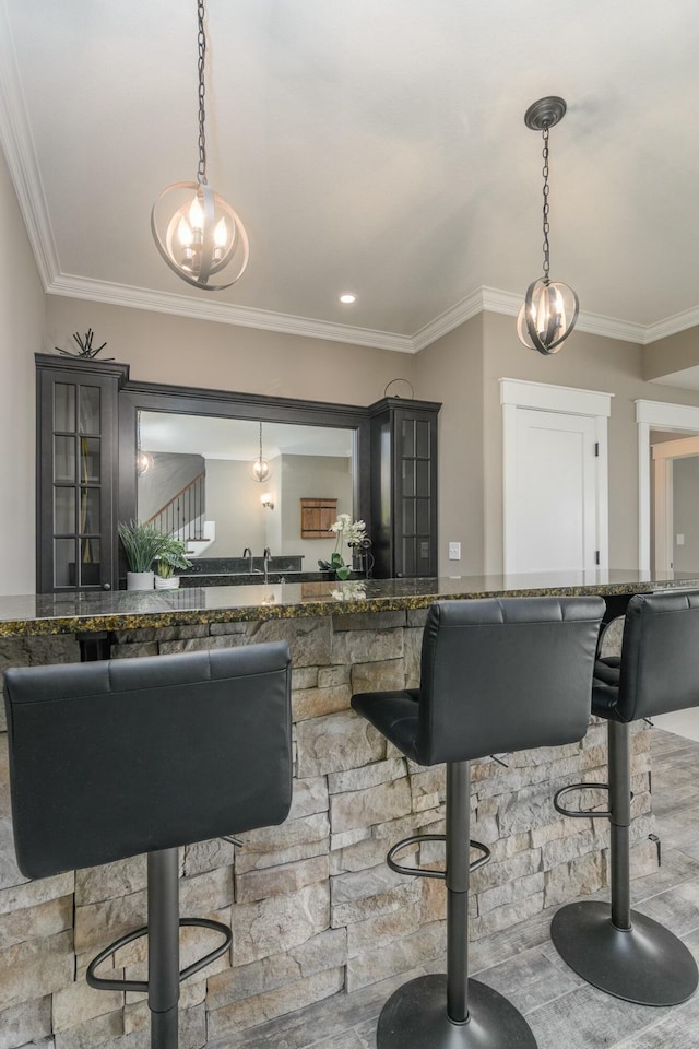 interior space featuring ornamental molding, dark stone counters, decorative light fixtures, and a kitchen breakfast bar