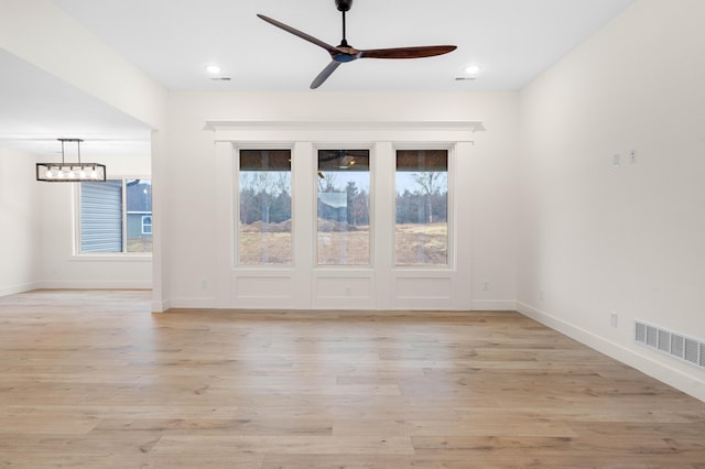 empty room featuring ceiling fan with notable chandelier and light hardwood / wood-style floors