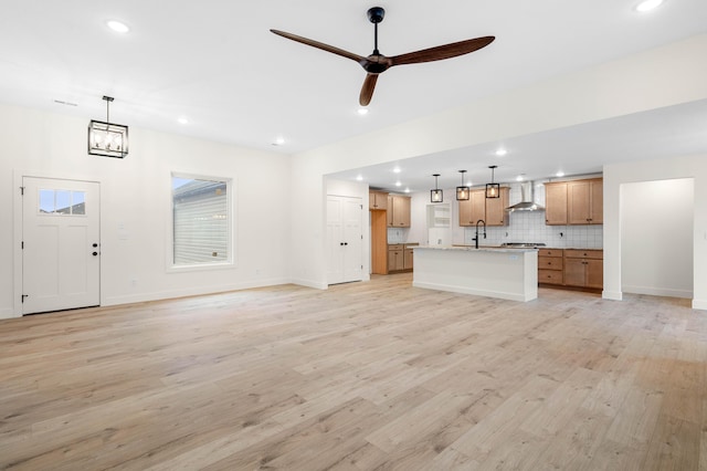 unfurnished living room with sink, ceiling fan with notable chandelier, and light wood-type flooring