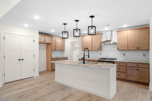 kitchen featuring a kitchen island with sink, decorative light fixtures, stainless steel range oven, and wall chimney exhaust hood