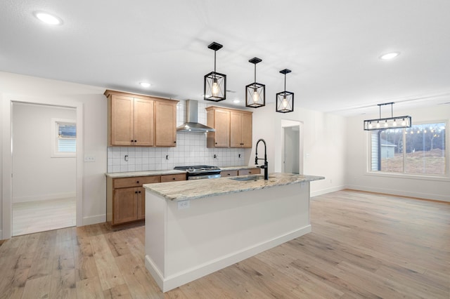 kitchen with pendant lighting, sink, a kitchen island with sink, stainless steel range with gas stovetop, and wall chimney range hood