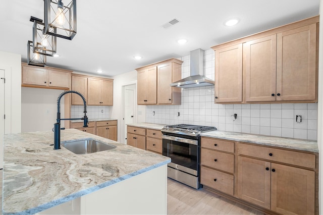 kitchen featuring sink, stainless steel range with gas stovetop, light stone countertops, wall chimney exhaust hood, and light wood-type flooring