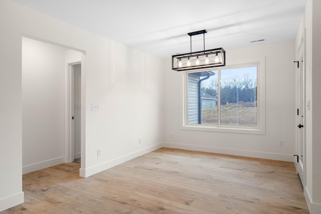 unfurnished dining area featuring an inviting chandelier and light wood-type flooring