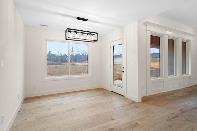 unfurnished dining area with a notable chandelier and light hardwood / wood-style flooring