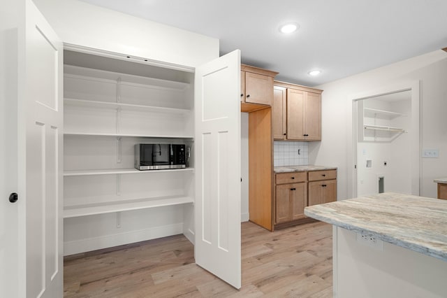 kitchen with backsplash, light stone counters, and light hardwood / wood-style flooring