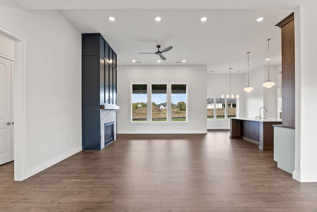 unfurnished living room with a fireplace, ceiling fan with notable chandelier, dark hardwood / wood-style floors, and sink