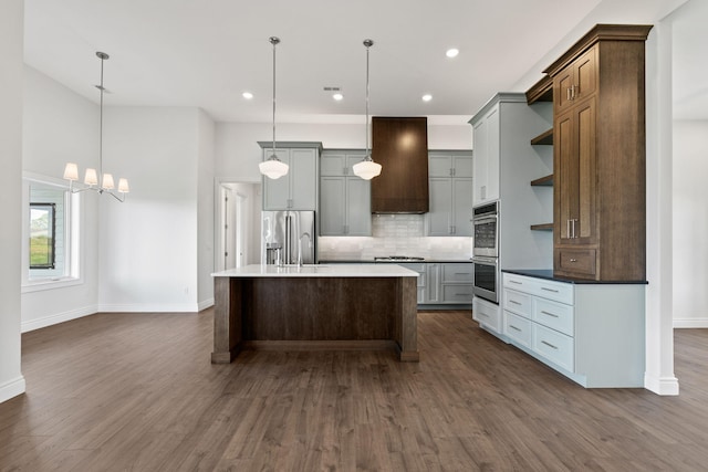 kitchen with gray cabinets, an island with sink, hanging light fixtures, and custom range hood