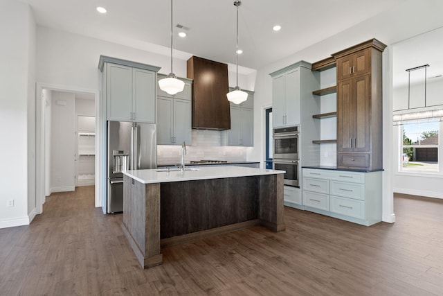 kitchen featuring pendant lighting, custom exhaust hood, a center island with sink, decorative backsplash, and stainless steel appliances