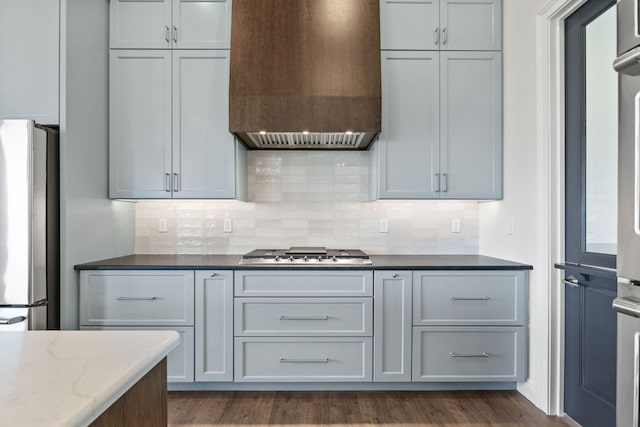 kitchen with light stone countertops, stainless steel appliances, tasteful backsplash, premium range hood, and gray cabinets