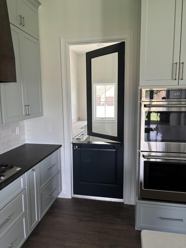 kitchen with tasteful backsplash, premium range hood, cooktop, stainless steel double oven, and dark wood-type flooring