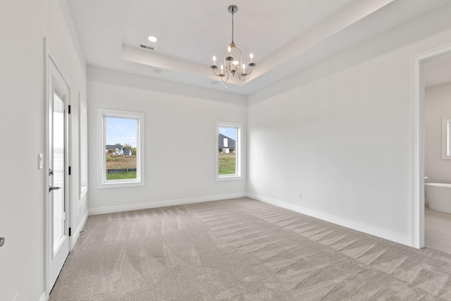 unfurnished room featuring a raised ceiling, a healthy amount of sunlight, light colored carpet, and an inviting chandelier